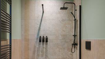 A shower area with a rain showerhead, handheld showerhead, and three bottles of shampoo.