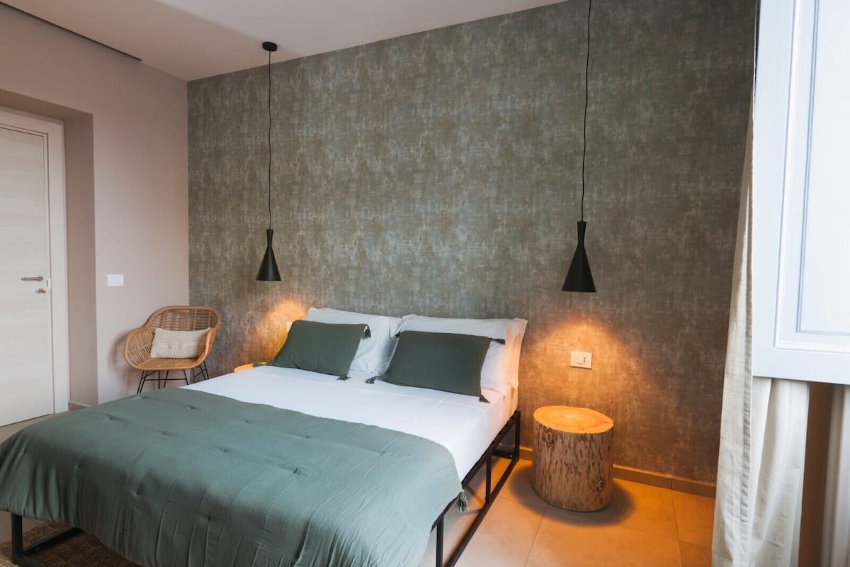 A bedroom with a bed, a chair, and a round wooden table.
