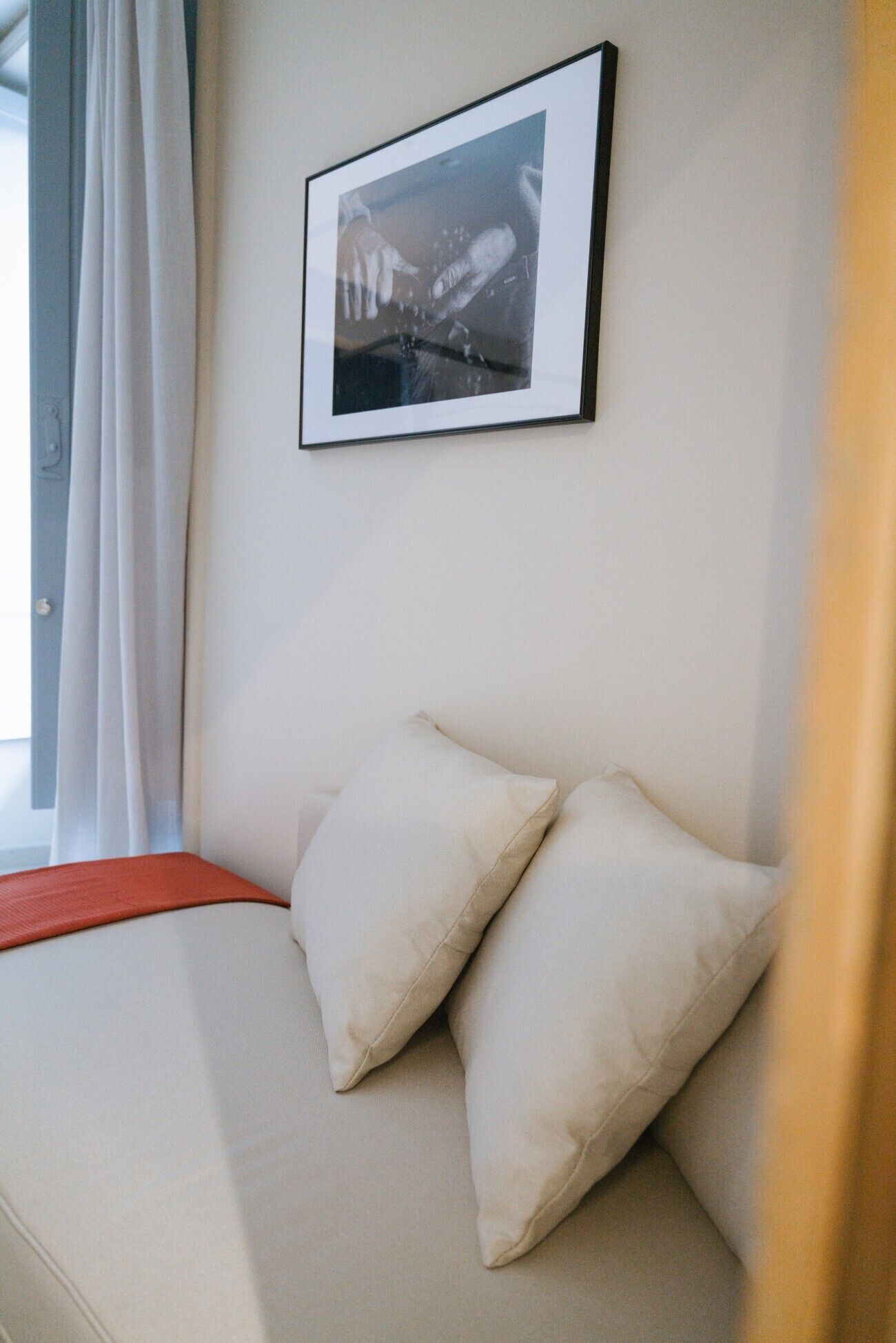 A room with a bed, two pillows, a framed picture on the wall, and a window with curtains.