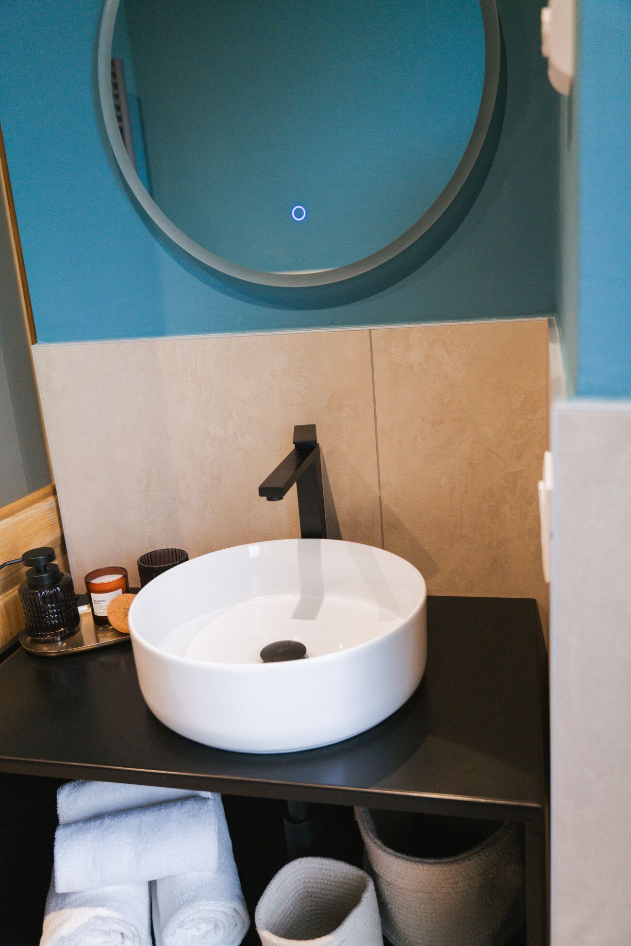 Un baño moderno con un lavamanos blanco, grifo negro y un espejo redondo encima.