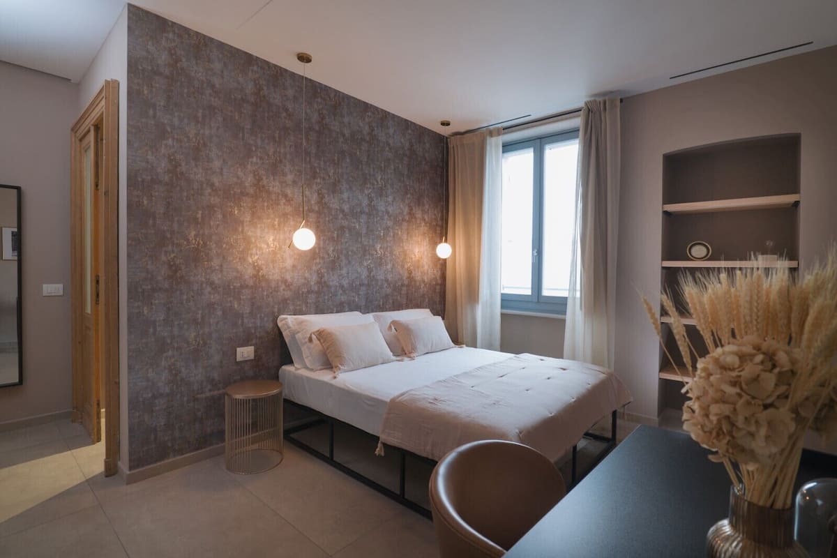A modern bedroom with a bed, bedside tables, a window, and a bookshelf.