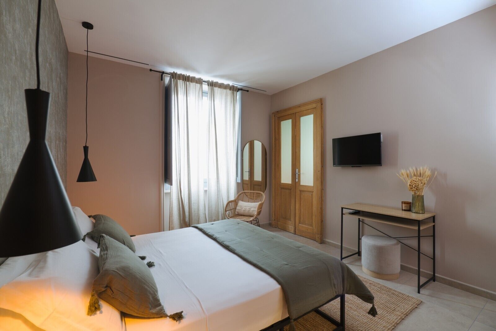 A bedroom with a bed, bedside table, TV, and a window with curtains.