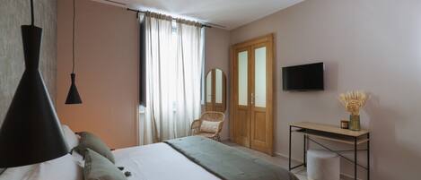 A bedroom with a bed, bedside table, TV, and a window with curtains.
