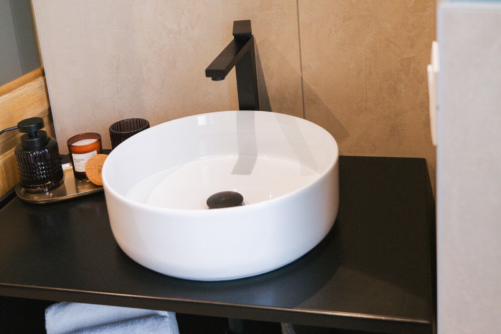 A white vessel sink with a black faucet on a black countertop.
