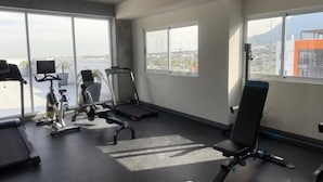 Ein Fitnessstudio mit Trainingsgeräten, großen Fenstern und Blick auf die Stadt.