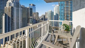 A balcony with a view of high-rise buildings, a white railing, and outdoor furniture. - Sky-High Luxury 3BR with Brickell City & Bay Views (Miami)