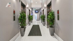 A modern hotel hallway with a central carpet, potted plants, and a television screen at the end. - Sky-High Luxury 3BR with Brickell City & Bay Views (Miami)