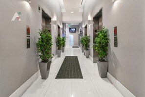 A modern hotel hallway with a central carpet, potted plants, and a television screen at the end. - Sky-High Luxury 3BR with Brickell City & Bay Views (Miami)