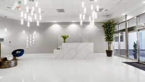 A modern reception area with a marble reception desk, hanging lights, a blue chair, and potted plants. - Sky-High Luxury 3BR with Brickell City & Bay Views (Miami)