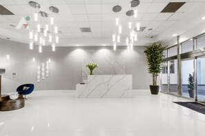 A modern reception area with a marble reception desk, hanging lights, a blue chair, and potted plants. - Sky-High Luxury 3BR with Brickell City & Bay Views (Miami)