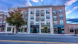 A multi-story building with a brick facade, large windows, and a tree in front.