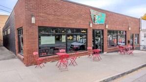 A brick building with a storefront, large windows, and red folding chairs outside.