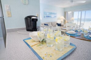 A dining area with a table set for a meal, featuring clear glasses with lemon slices, plates, and a tray. - "Sunset Coast Retreat" – King Bed – Gulf Front – Bonita Springs (Bonita Springs)