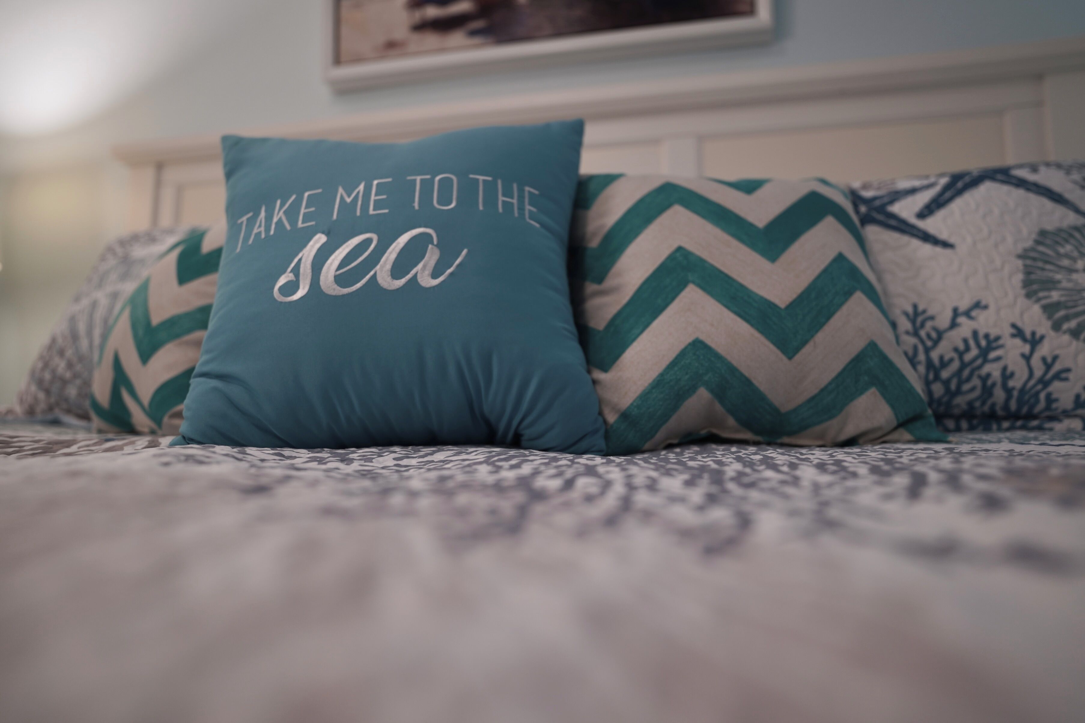 En säng med mönstrat sänglinne och en kudde med texten ”TA MIG TILL HAVET”.