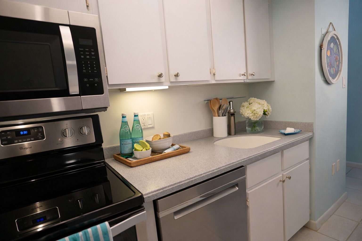Una cocina moderna con electrodomésticos de acero inoxidable, una encimera blanca y un lavamanos.