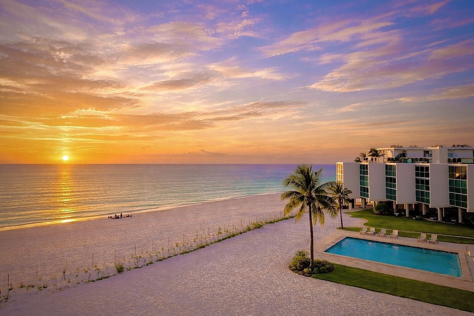 A beachfront hotel with a pool, palm trees, and a sunset view.