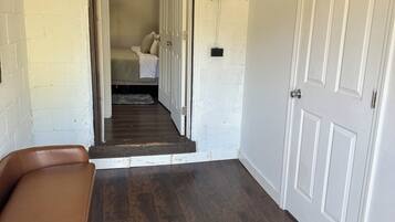 Un couloir avec un banc en cuir marron, une porte blanche et un escalier menant à une chambre à coucher équipée d’un lit et d’une table de chevet.