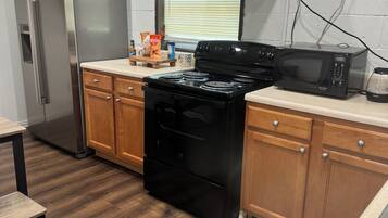 Une cuisine équipée d’un réfrigérateur en acier inoxydable, d’une cuisinière noire, de meubles de rangement en bois et d’une fenêtre avec des stores.