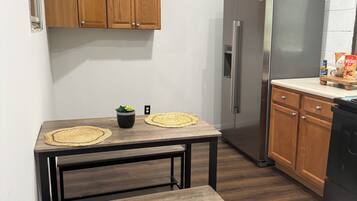 Une cuisine avec des meubles en bois, un réfrigérateur en acier inoxydable, une table à manger en bois avec un banc, et une plante en pot.