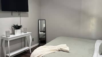 Une chambre à coucher comprenant un lit, un ventilateur de plafond, une télévision, un miroir et une console sur laquelle sont disposés des objets décoratifs.