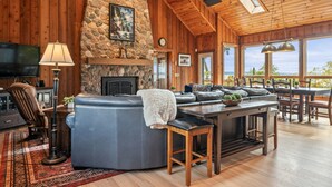 A cozy living room with a stone fireplace, wooden ceiling, and large windows overlooking a scenic view. - Private FLX Retreat | 200' Seneca Lakefront | Pool (Geneva)