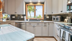 A modern kitchen with grey cabinets, a large window, and stainless steel appliances. - Private FLX Retreat | 200' Seneca Lakefront | Pool (Geneva)