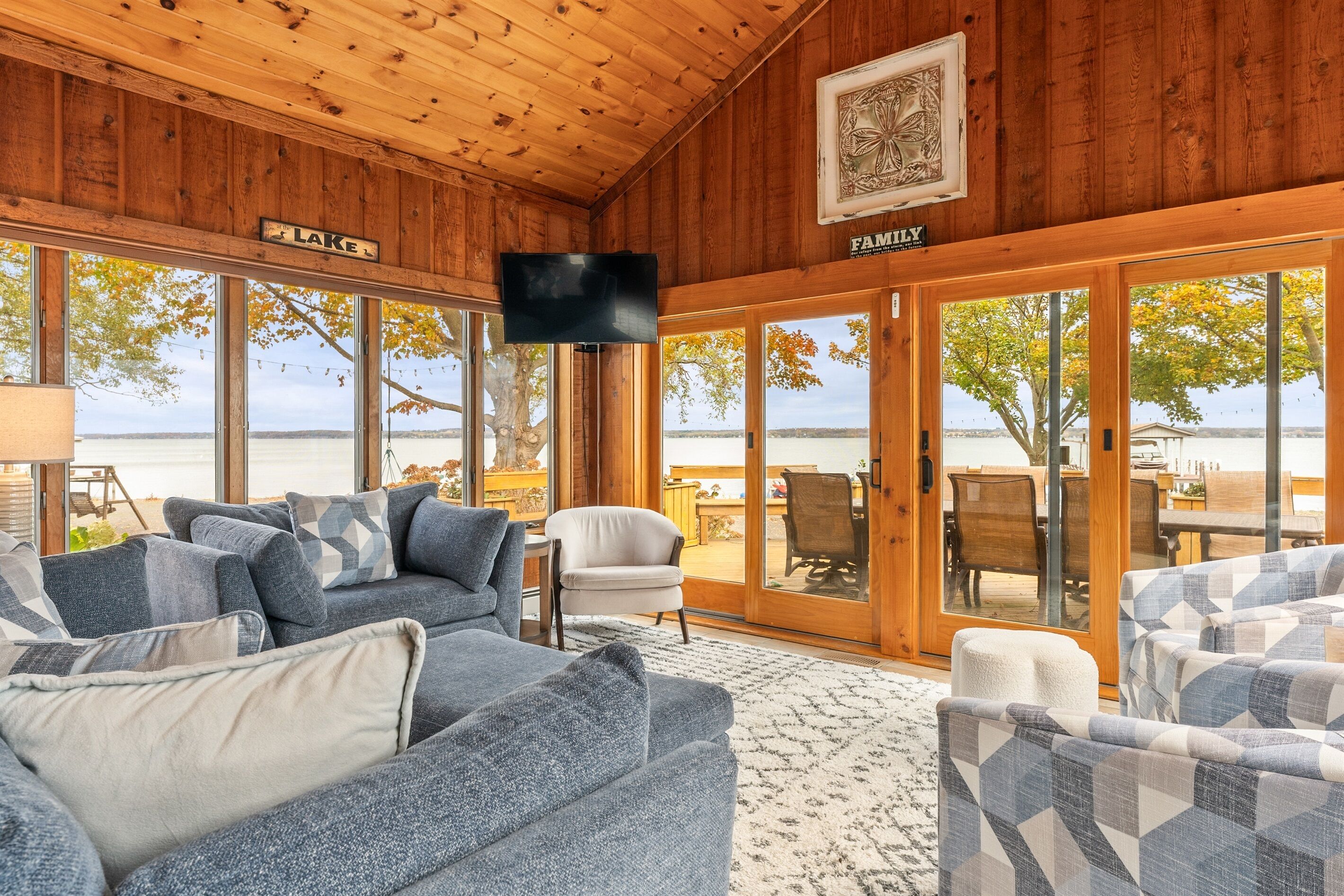 Un chalet confortable doté d’une grande fenêtre donnant sur un lac, meublé de canapés à motifs bleus et blancs et d’un téléviseur à écran plat fixé au plafond.