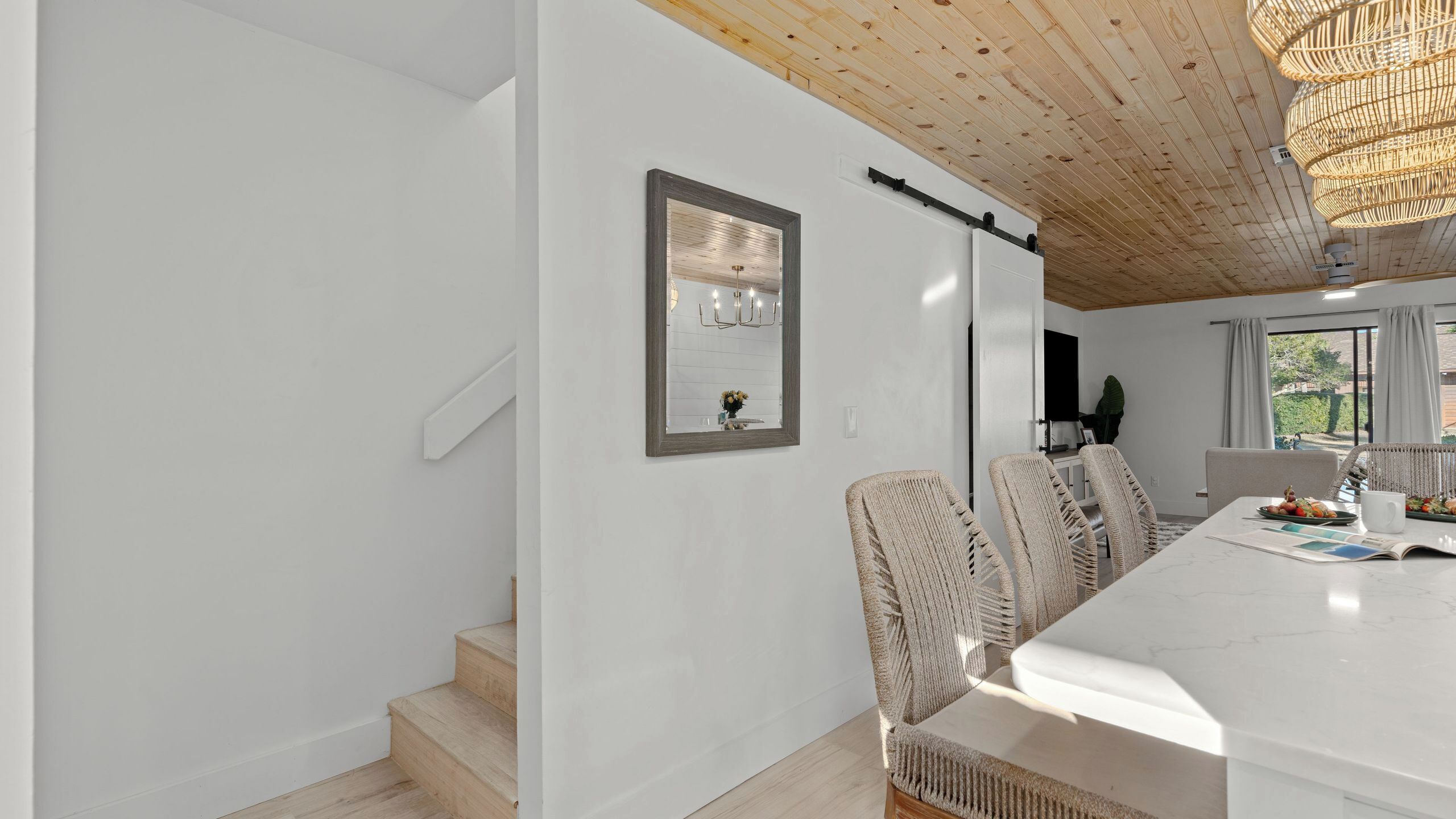 Ein modernes Interieur mit einer Treppe, einem Essbereich mit weißem Tisch und Stühlen sowie einem großen Spiegel an der Wand.
