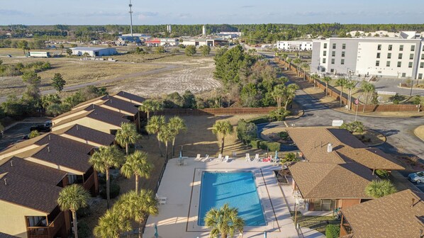 A residential area with a swimming pool, palm trees, and a large building in the background. - Sandbar Serenade by Avantstay Beachside Home + Pool + Tennis Court + Beach Access + Near Pier Park (Panama City Beach)