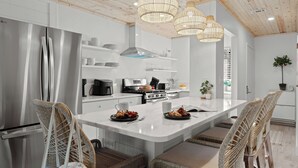 A modern kitchen with a stainless steel refrigerator, a built-in oven, and a large island with seating. - Sandbar Serenade by Avantstay Beachside Home + Pool + Tennis Court + Beach Access + Near Pier Park (Panama City Beach)