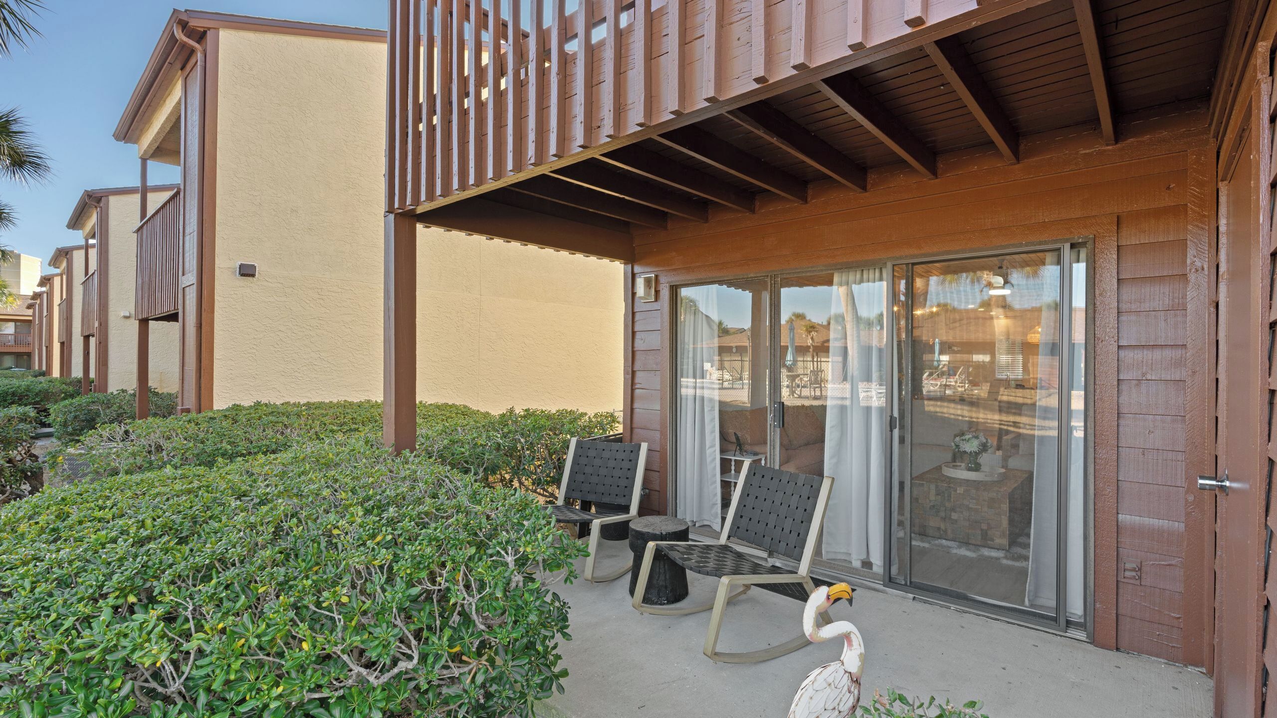 A hotel with a covered outdoor seating area, a pool, and a flamingo statue.