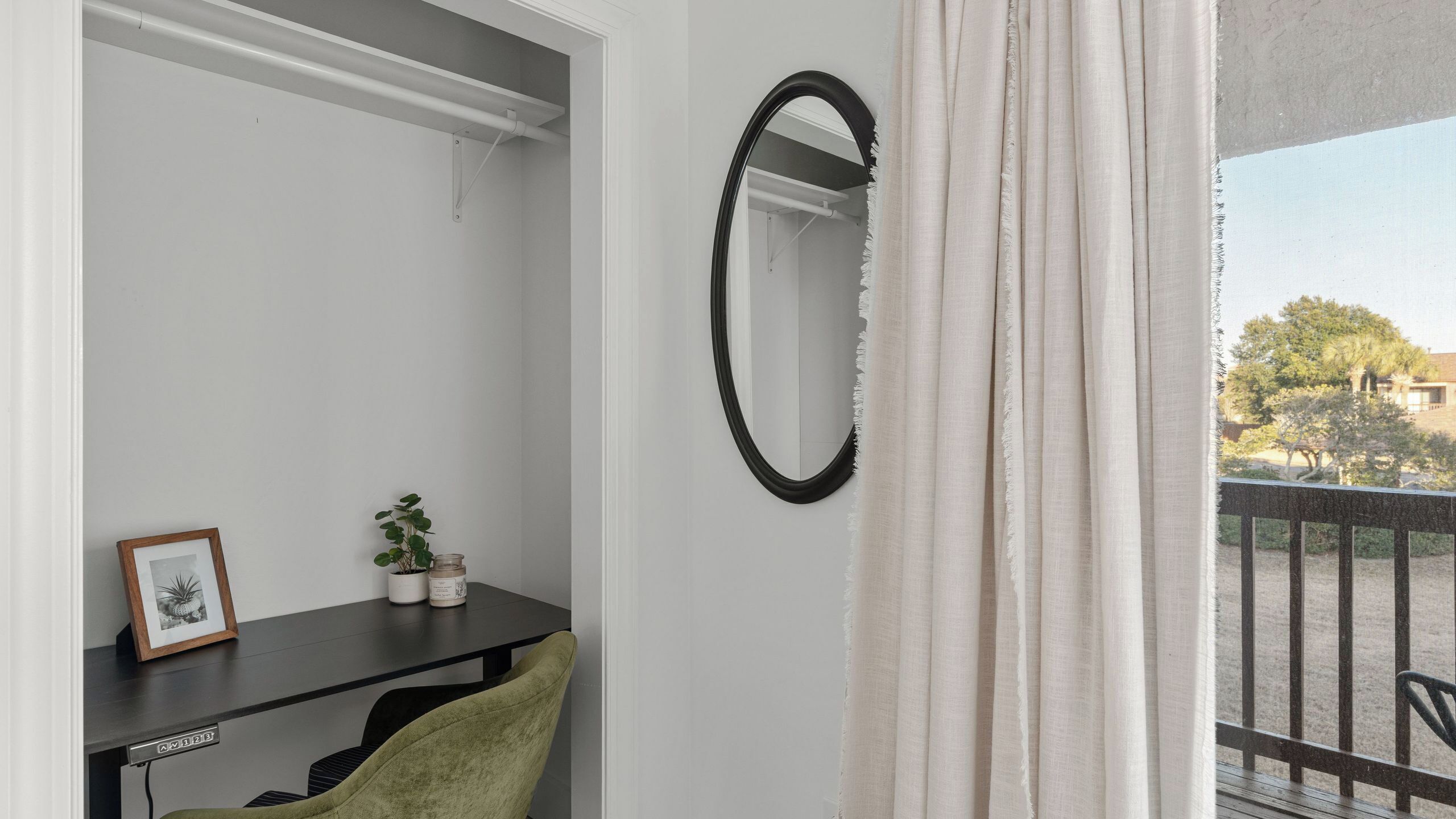A room with a desk, chair, framed picture, potted plant, and a mirror on the wall.