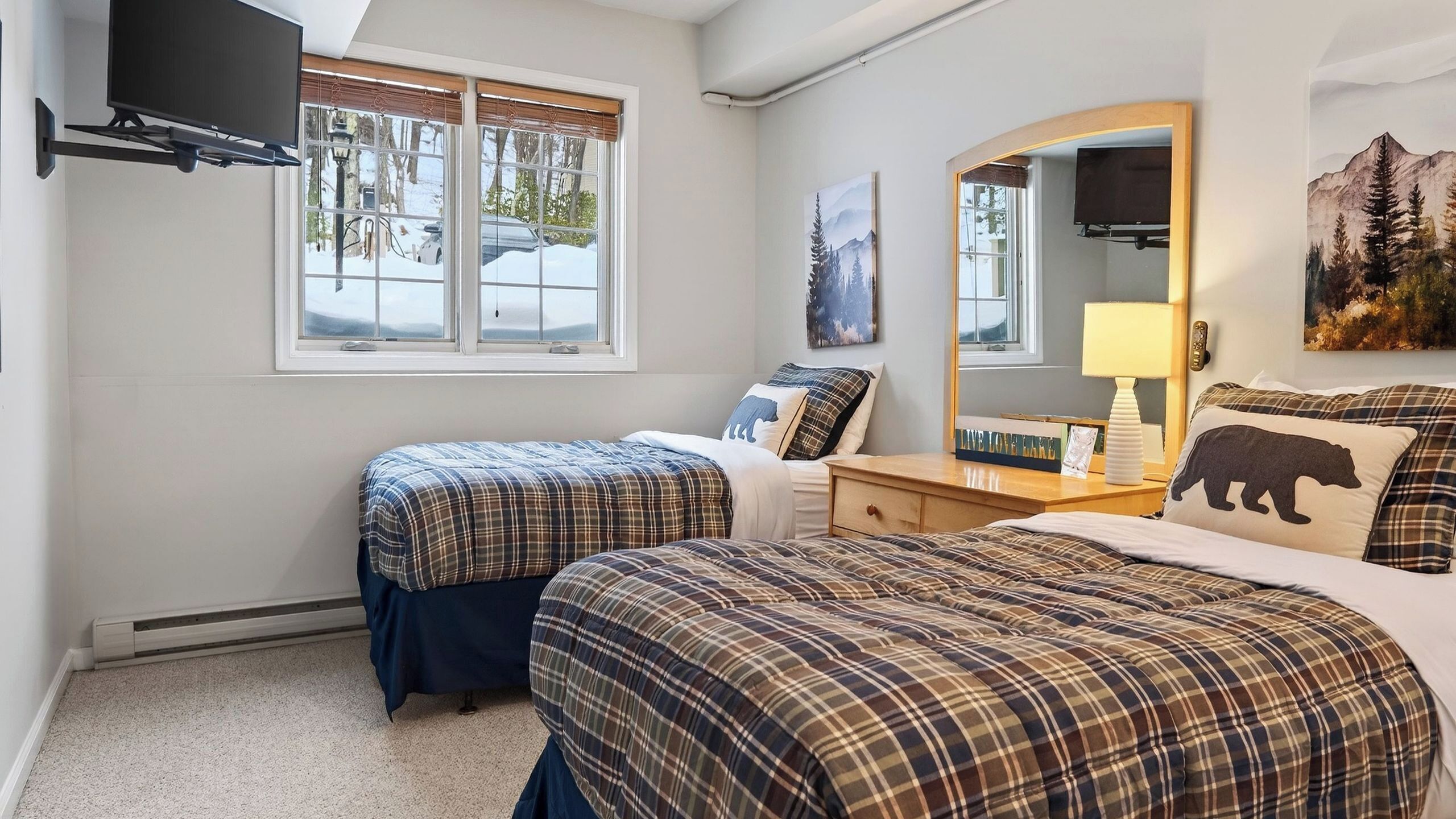 A bedroom with two beds, a dresser, a mirror, and a TV mounted on the wall.