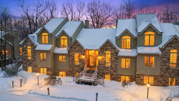 Une maison en pierre à plusieurs étages, dont le toit est recouvert de neige, avec de nombreuses fenêtres et une entrée centrale surmontée d’un escalier.