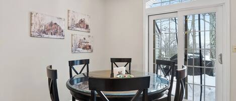 A dining area with a round glass table, four chairs, and three rustic barn-themed paintings on the wall.