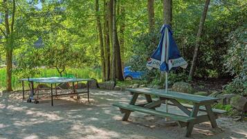 A picnic table and umbrella in a forested area with a car nearby.