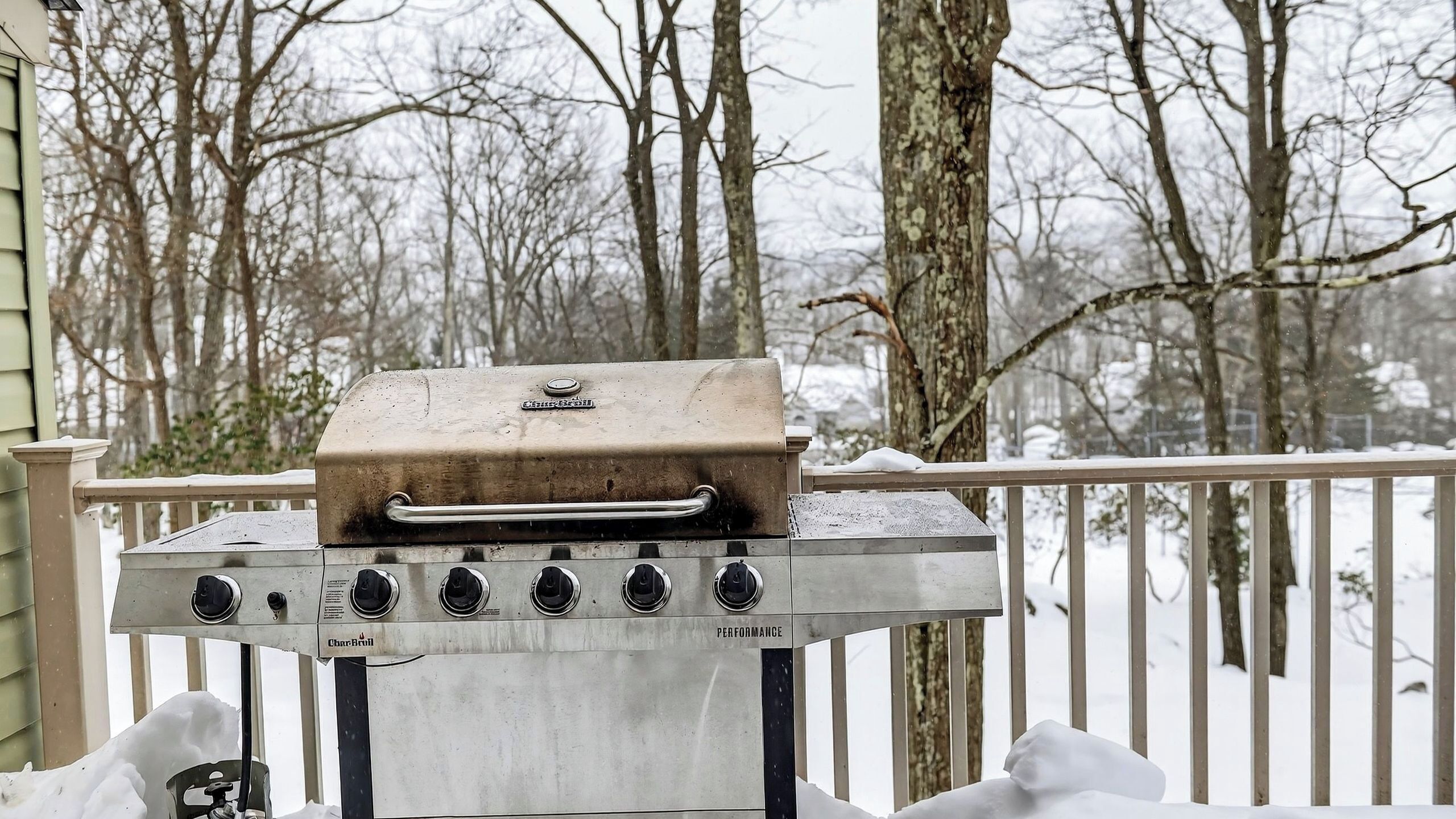 A Char-Bri grill on a balcony with a snow-covered deck and bare trees in the background.