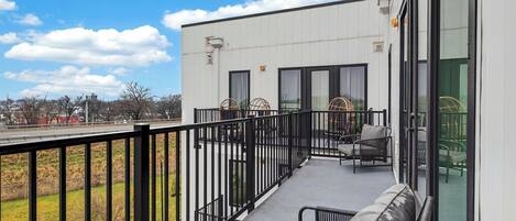 A balcony with a sofa, chairs, and a railing overlooking a grassy area.