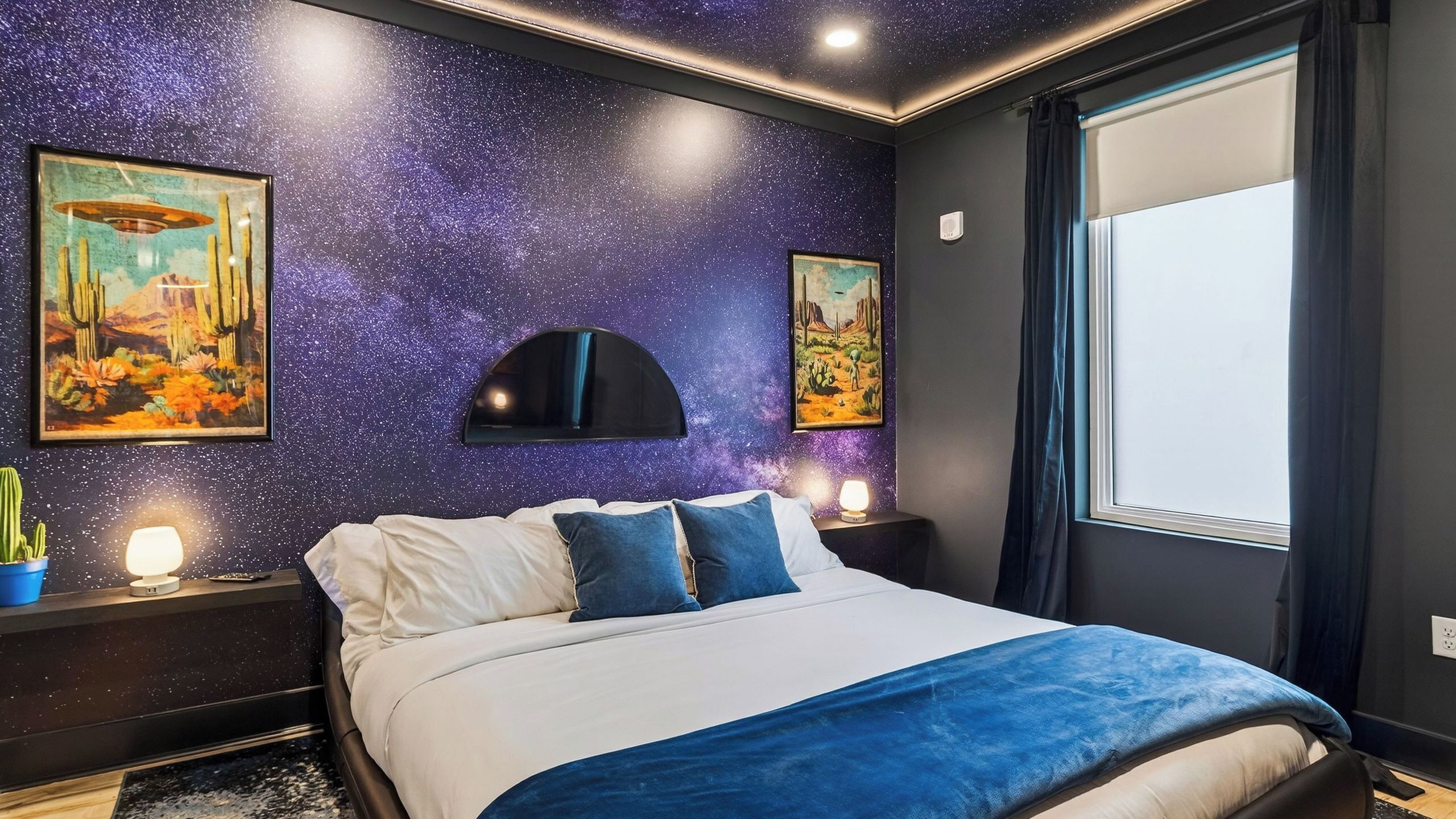 Une chambre avec un mur décoré de motifs étoilés, un lit avec une literie blanche et bleue, et deux tableaux accrochés au mur.