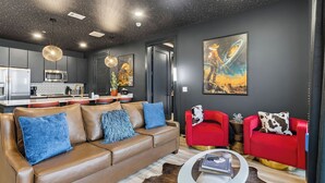 Ein modernes Wohnzimmer mit einem Ledersofa, roten Sesseln, einem Glastisch und einer Küche im Hintergrund.