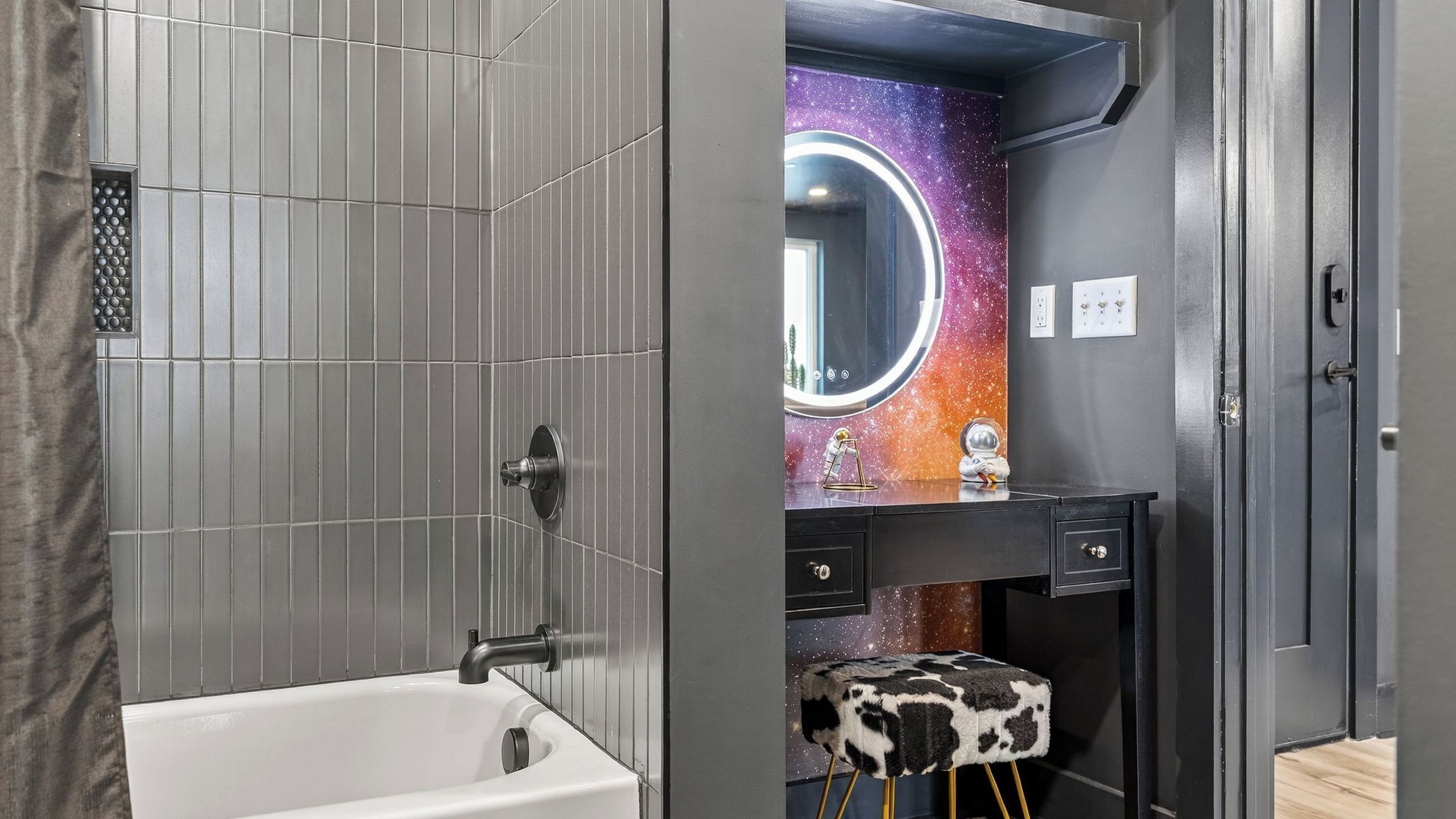 Een moderne badkamer met een grote spiegel, een muur met een sterrenstelsel thema en een klein krukje.