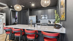 Una cocina moderna con una isla central, taburetes de bar, electrodomésticos de acero inoxidable y detalles decorativos.