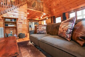 A cozy cabin interior with a wooden staircase, a sofa with patterned cushions, a bookshelf, and a kitchen area. - Smoky Elk Cabin, pet friendly with hot tub! (Whittier)