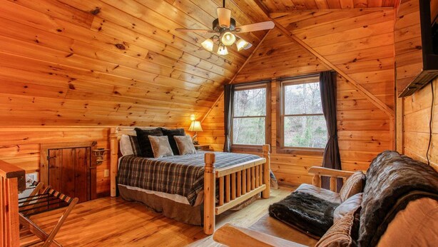 L’intérieur d’un chalet accueillant, avec un lit, un banc en bois et une fenêtre donnant sur la forêt.