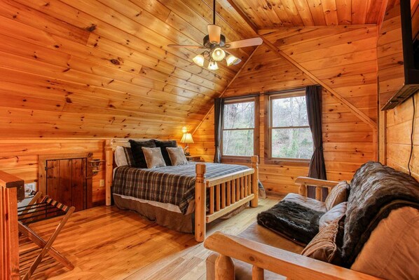 A cozy cabin interior with a bed, a wooden bench, and a window with a view of the forest. - Smoky Elk Cabin, pet friendly with hot tub! (Whittier)