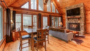 L’intérieur d’une cabane en rondins, avec une cheminée en pierre, des meubles en bois et de grandes fenêtres.