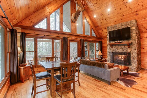 A log cabin interior with a stone fireplace, wooden furniture, and large windows. - Smoky Elk Cabin, pet friendly with hot tub! (Whittier)