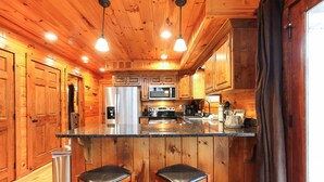 L’intérieur d’un chalet en bois comprend une cuisine équipée d’un réfrigérateur, d’un four à micro-ondes et de tabourets de bar.