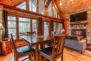 A log cabin interior with a dining table, chairs, a fireplace, and a television mounted on a stone wall. - Smoky Elk Cabin, pet friendly with hot tub! (Whittier)