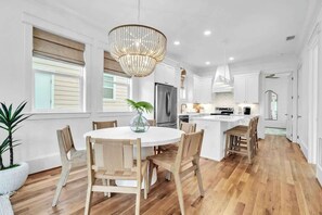 Une cuisine moderne avec une table de salle à manger ronde, des chaises en bois, un lustre et un grand îlot central.